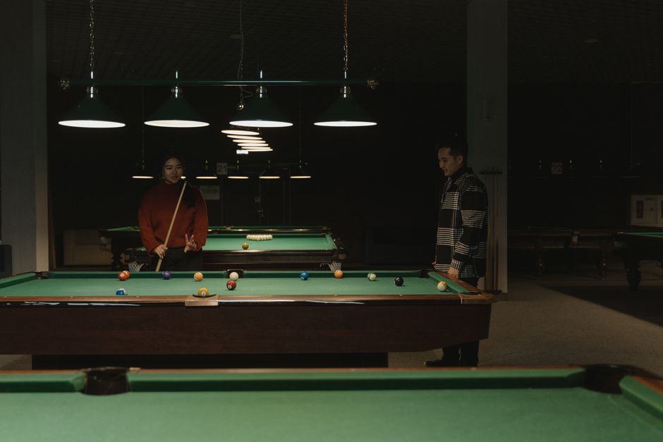 Two people playing pool at a table in a dimly lit hall